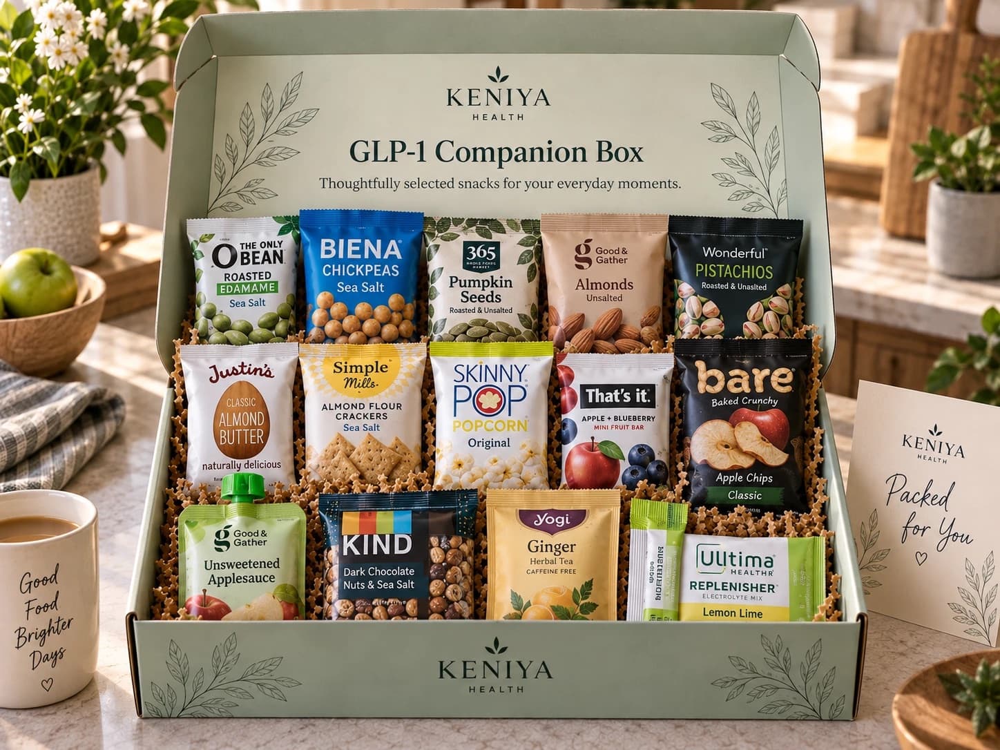 Example GLP-1 Companion Box of 14 snacks: roasted edamame, chickpeas, pumpkin seeds, almonds, pistachios, almond butter, almond flour crackers, popcorn, a mini fruit bar, apple chips, an applesauce pouch, a nut bar, ginger tea and an electrolyte stick